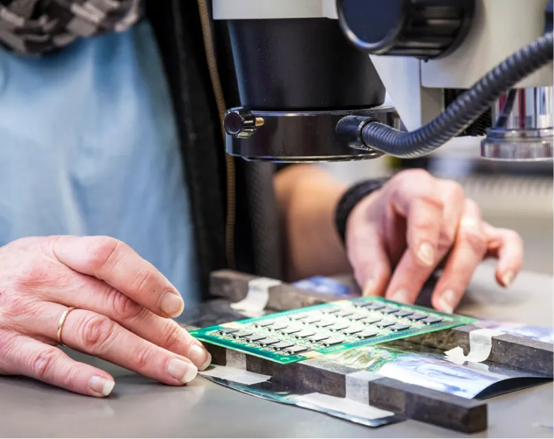Technician inspecting lead-free solder joints on a PCB for quality control.