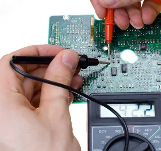 Technician testing gaming console PCB with a multimeter for voltage issues