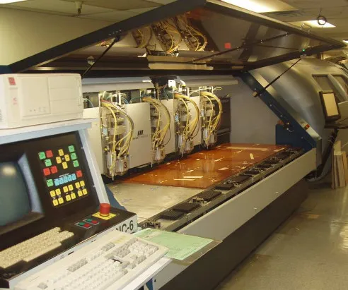 Operator in PPE using laser drilling equipment for PCB manufacturing.