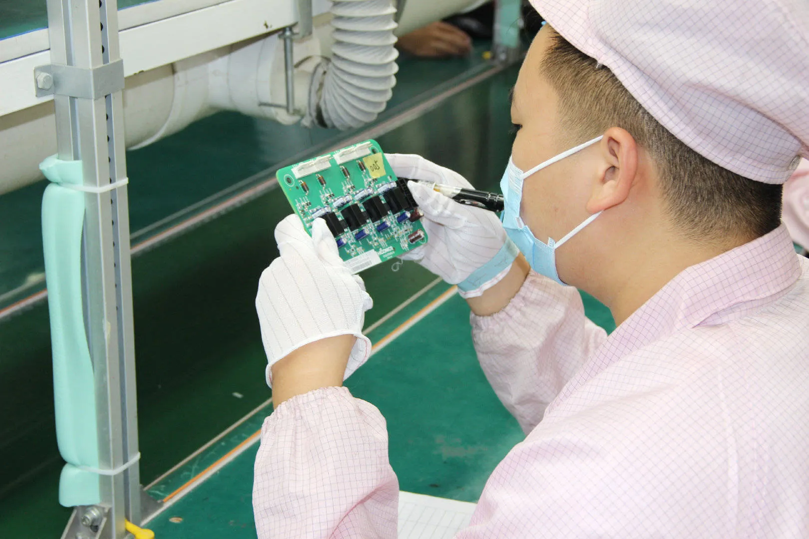 Technician performing quality control inspection on PCBs in mass production.