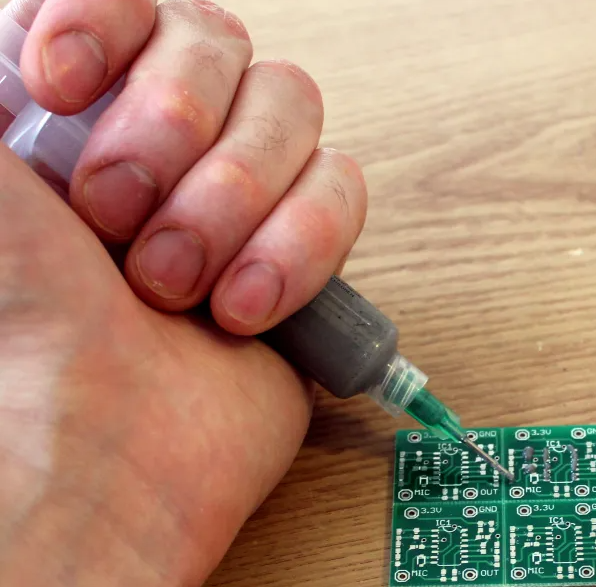 Engineer applying solder paste with a syringe dispenser.