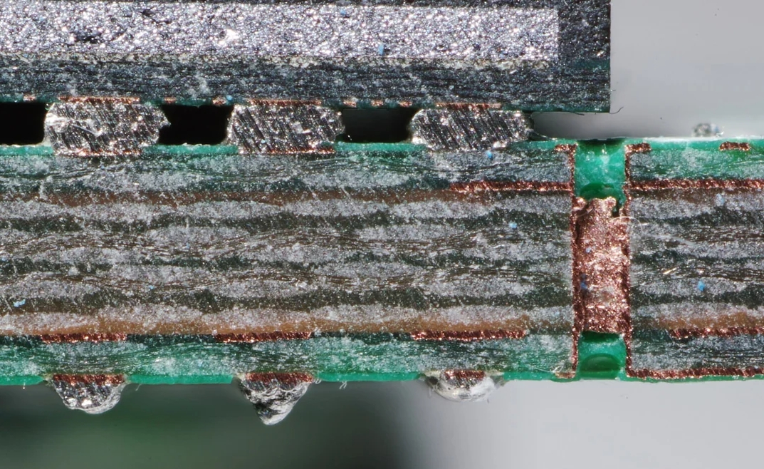 PCB cross-section under microscope revealing internal layers and vias.