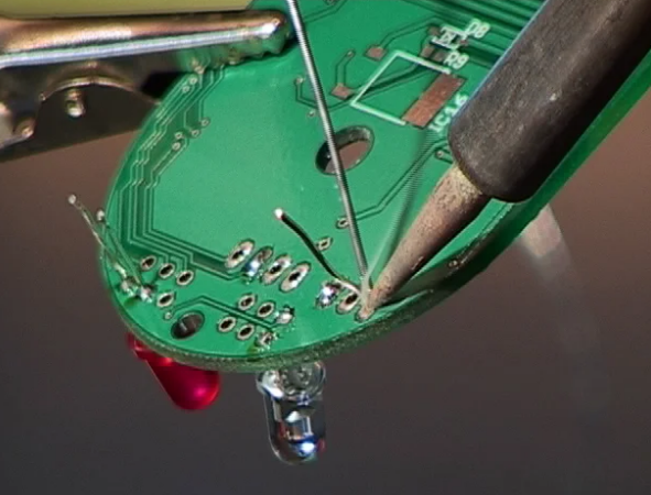 Close-up of through-hole assembly tutorial showing soldered resistor on PCB
