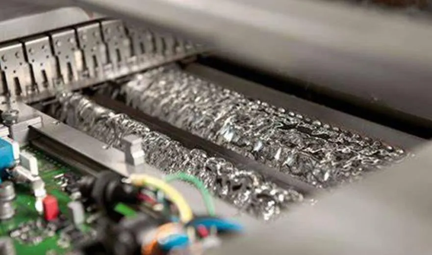 Wave soldering machine creating molten solder wave for PCB assembly.