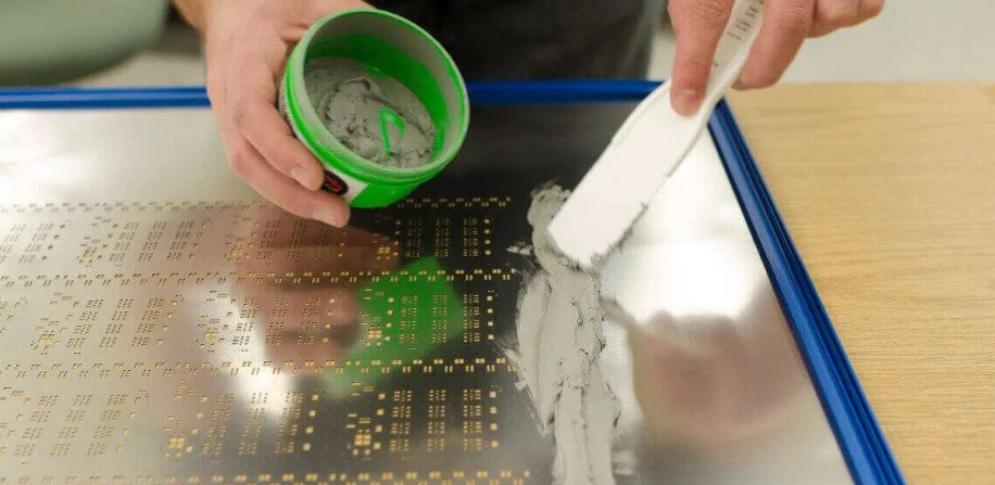 Applying solder paste using homemade stencil for electronics projects.
