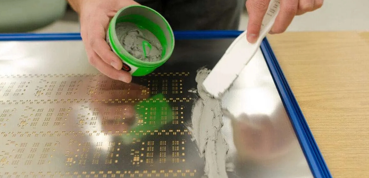 Applying solder paste using a squeegee over a stencil on a PCB.