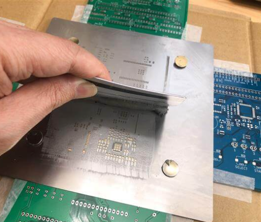 "SMT stencil aligned with PCB in a printer, showing fiducial marks for precision."