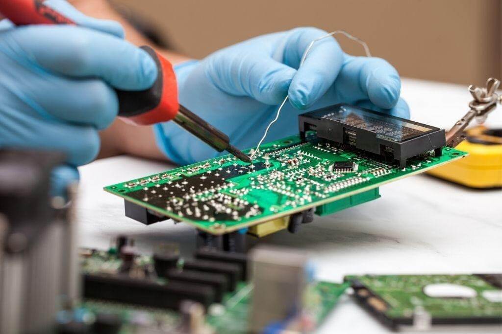 Technician using manual pick and place tools for SMT assembly on a PCB.
