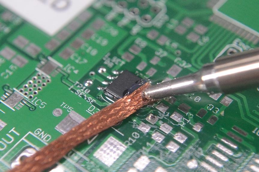 Using solder wick to remove a solder bridge on a PCB.