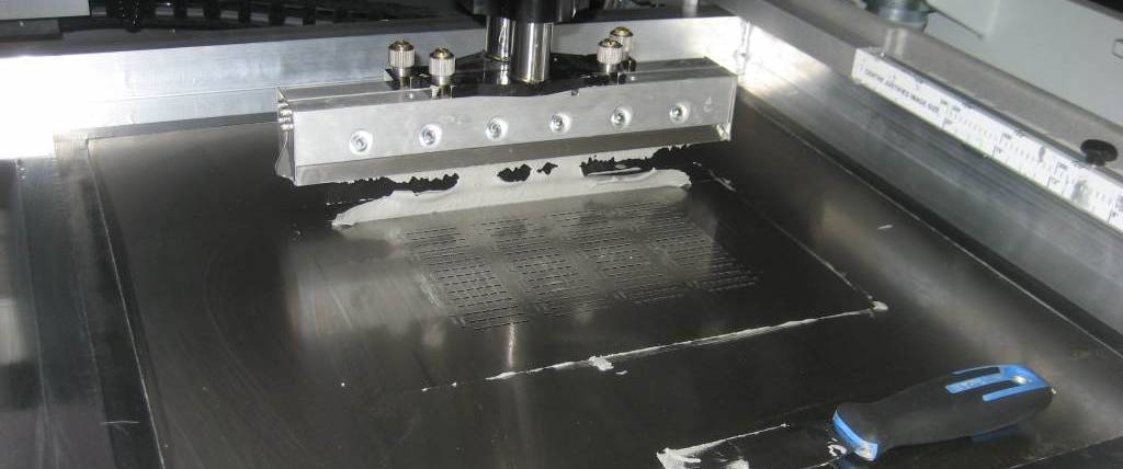 Squeegee blade pushing solder paste through stencil apertures onto PCB